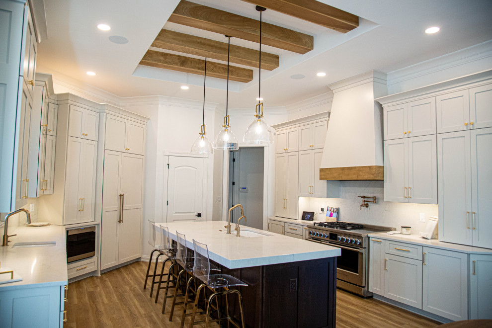 Large transitional u-shaped eat-in kitchen in Indianapolis with an undermount sink, shaker cabinets, white cabinets, quartz benchtops, white splashback, engineered quartz splashback, stainless steel appliances, laminate floors, with island, blue floor, white benchtop and exposed beam.