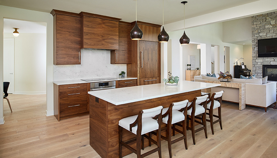 This is an example of a large midcentury l-shaped open plan kitchen in Grand Rapids with an undermount sink, flat-panel cabinets, dark wood cabinets, quartz benchtops, white splashback, marble splashback, stainless steel appliances, light hardwood floors, with island, brown floor and white benchtop.