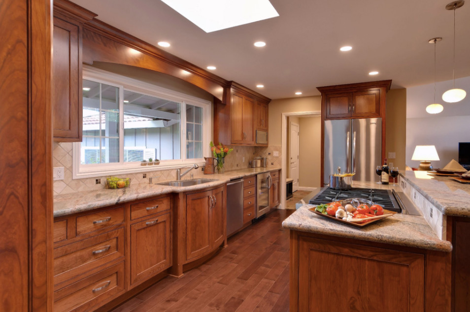 This is an example of a large traditional l-shaped open plan kitchen in Houston with a double-bowl sink, recessed-panel cabinets, medium wood cabinets, granite benchtops, beige splashback, ceramic splashback, stainless steel appliances, medium hardwood floors, with island, brown floor and beige benchtop.