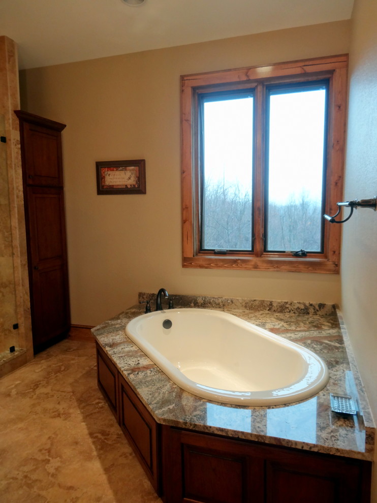 Design ideas for an expansive country master bathroom in Charlotte with an undermount sink, raised-panel cabinets, dark wood cabinets, granite benchtops, a corner tub, an alcove shower, a two-piece toilet, beige tile, ceramic tile, beige walls and ceramic floors.