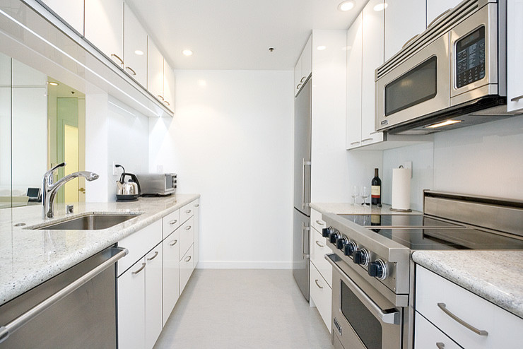 Photo of a mid-sized modern galley kitchen pantry in San Francisco with a drop-in sink, flat-panel cabinets, white cabinets, granite benchtops, white splashback, stainless steel appliances and with island.