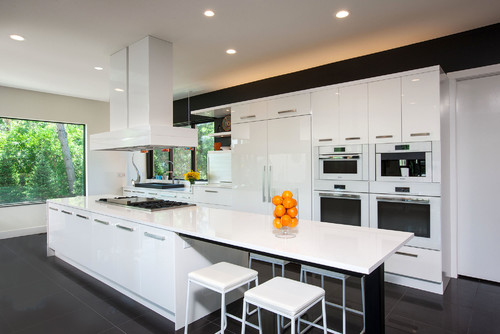 High-gloss white RTA cabinets in a modern kitchen with a long waterfall island, gas cooktop, built-in wall ovens, and panel-ready fridge.