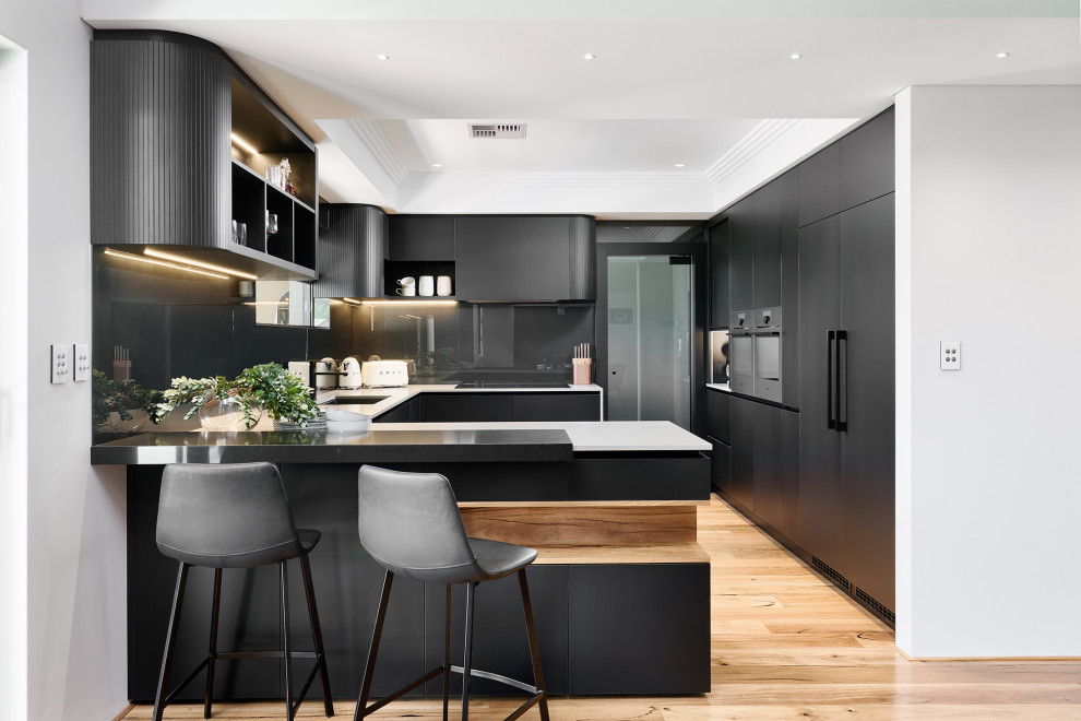 Foto på ett stort funkis grå kök, med en undermonterad diskho, släta luckor, svarta skåp, bänkskiva i kvarts, svart stänkskydd, glaspanel som stänkskydd, svarta vitvaror, ljust trägolv, en köksö och brunt golv