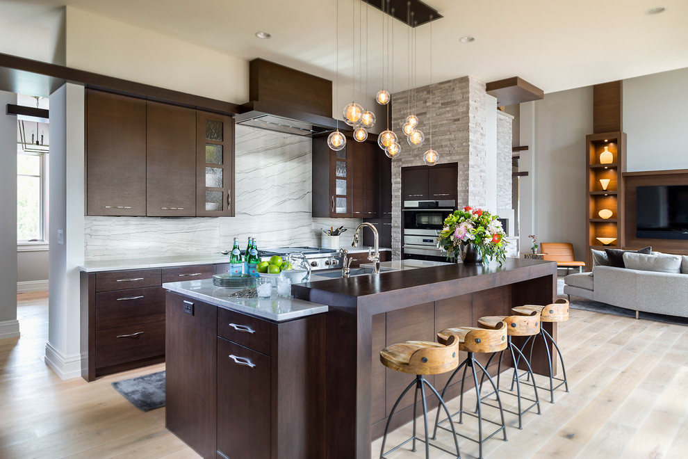 This is an example of an expansive contemporary eat-in kitchen in Minneapolis with a farmhouse sink, flat-panel cabinets, dark wood cabinets, quartzite benchtops, white splashback, stone slab splashback, stainless steel appliances, light hardwood floors and with island.