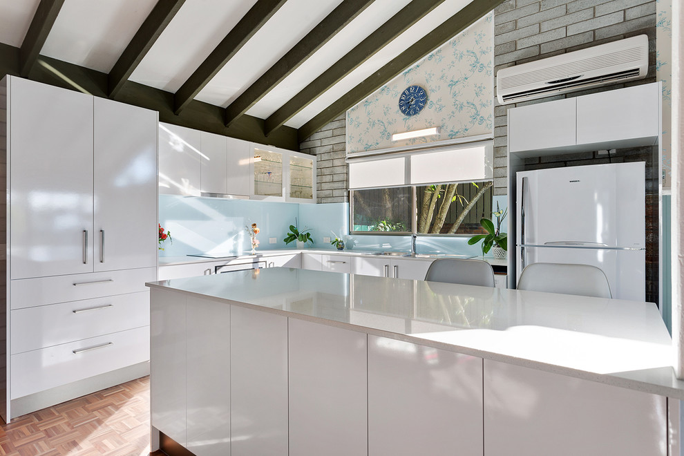 Photo of a mid-sized traditional eat-in kitchen in Gold Coast - Tweed with flat-panel cabinets, white cabinets, quartz benchtops, blue splashback, glass sheet splashback, with island and white benchtop.