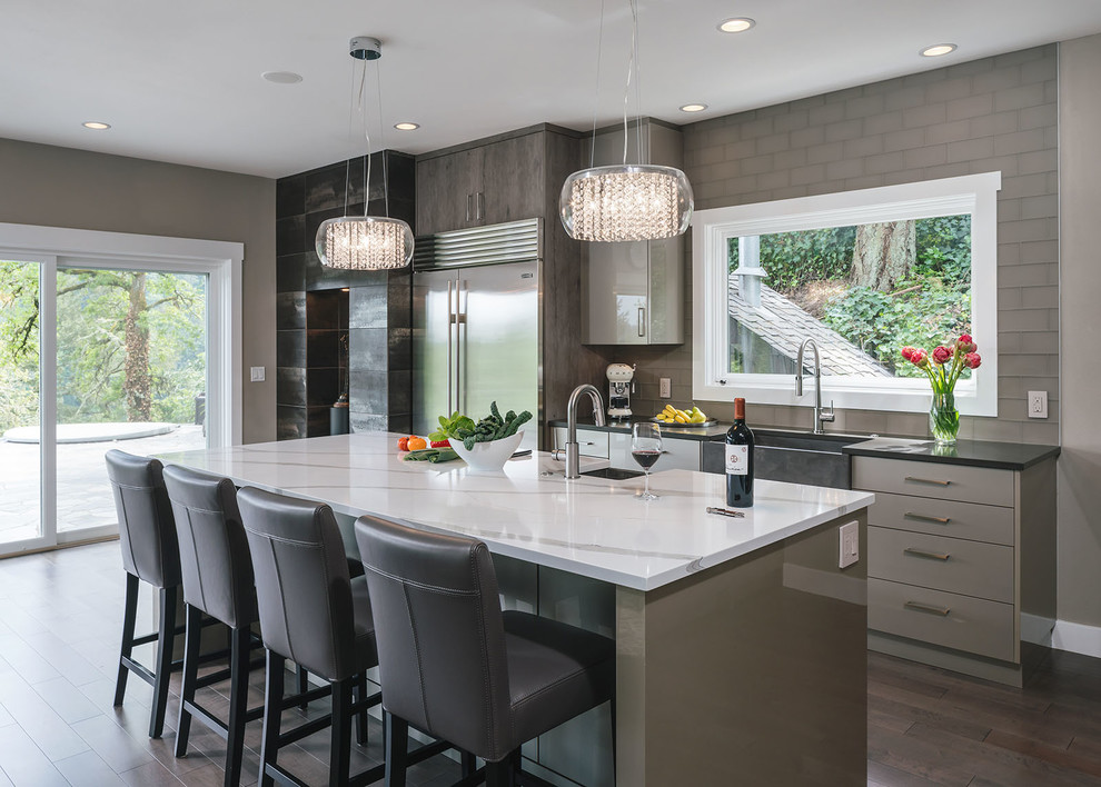 Inspiration for a large contemporary kitchen in Portland with a farmhouse sink, flat-panel cabinets, quartzite benchtops, glass tile splashback, stainless steel appliances, with island, grey cabinets, grey splashback, dark hardwood floors and black benchtop.