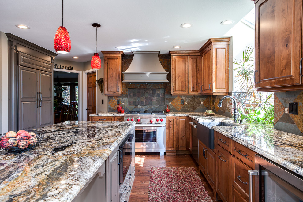 This is an example of a large traditional u-shaped open plan kitchen in Denver with a farmhouse sink, raised-panel cabinets, medium wood cabinets, granite benchtops, multi-coloured splashback, terra-cotta splashback, stainless steel appliances, medium hardwood floors, with island, brown floor and brown benchtop.