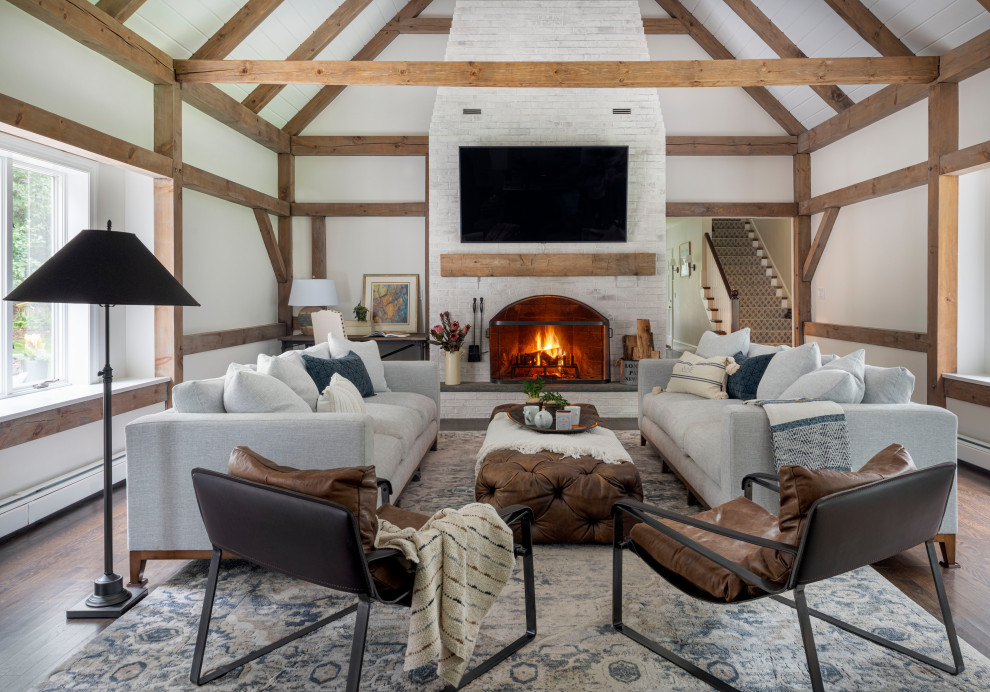 This is an example of an expansive country open plan games room in Boston with white walls, dark hardwood flooring, a standard fireplace, a brick fireplace surround, a wall mounted tv, brown floors, exposed beams and a chimney breast.