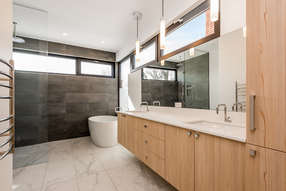 Large contemporary master bathroom in Ottawa with flat-panel cabinets, light wood cabinets, a freestanding tub, an open shower, a one-piece toilet, gray tile, stone tile, white walls, marble floors, an undermount sink, engineered quartz benchtops, white floor and an open shower.