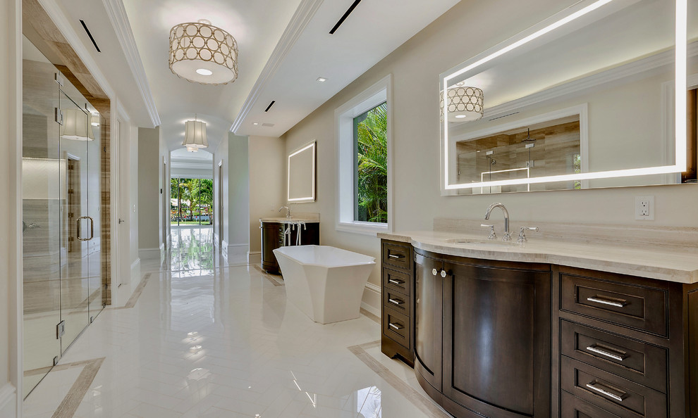 Inspiration for an expansive mediterranean master bathroom in Miami with beaded inset cabinets, medium wood cabinets, a freestanding tub, a double shower, a one-piece toilet, beige tile, marble, beige walls, marble floors, an undermount sink, marble benchtops, white floor, a hinged shower door and beige benchtops.