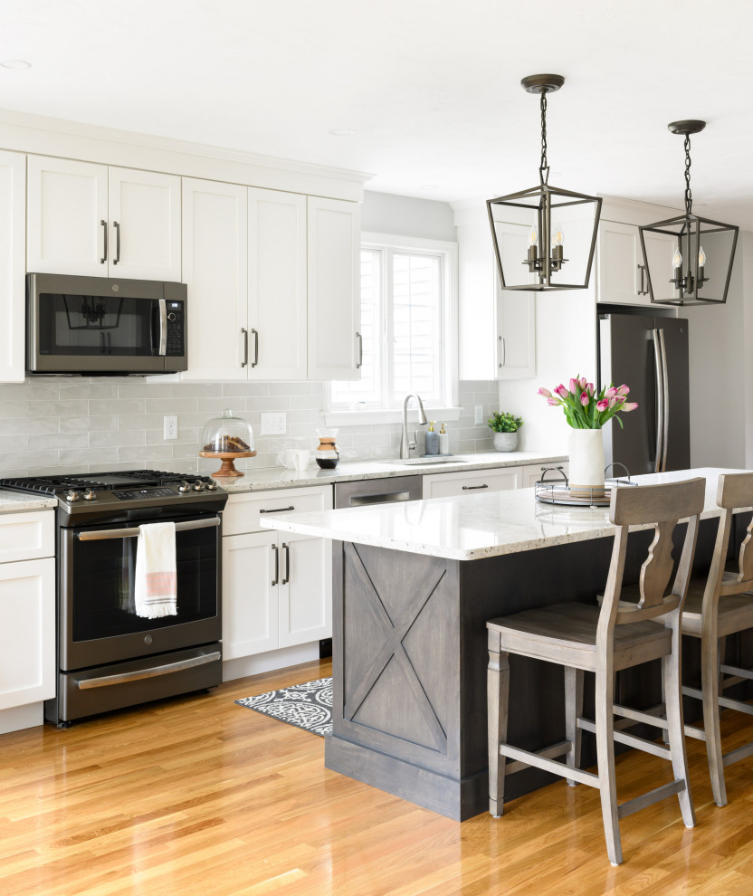 Transitional galley kitchen in Boston with an undermount sink, shaker cabinets, white cabinets, grey splashback, subway tile splashback, stainless steel appliances, medium hardwood floors, with island, brown floor and white benchtop.