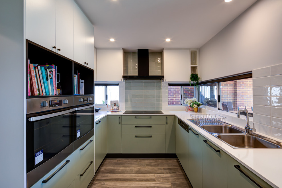 Inspiration for a contemporary u-shaped kitchen in Perth with white benchtop, a double-bowl sink, flat-panel cabinets, green cabinets, stainless steel appliances and brown floor.