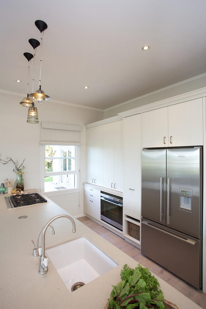 Design ideas for a small beach style galley eat-in kitchen in Auckland with a farmhouse sink, recessed-panel cabinets, white cabinets, quartz benchtops, stainless steel appliances, with island and light hardwood floors.