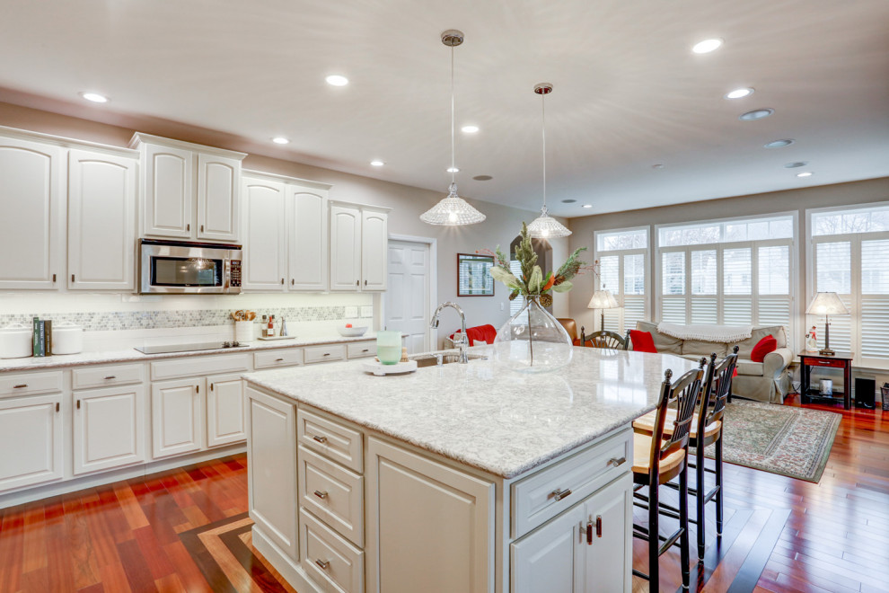 Inspiration for a large timeless l-shaped medium tone wood floor and brown floor open concept kitchen remodel in Other with an undermount sink, raised-panel cabinets, white cabinets, quartz countertops, white backsplash, ceramic backsplash, stainless steel appliances, an island and white countertops