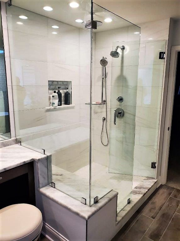 This is an example of a medium sized classic ensuite bathroom in Chicago with raised-panel cabinets, dark wood cabinets, a freestanding bath, a corner shower, a one-piece toilet, white tiles, stone tiles, white walls, wood-effect flooring, a submerged sink, engineered stone worktops, brown floors, a hinged door, multi-coloured worktops, a shower bench, double sinks, a built in vanity unit and a vaulted ceiling.
