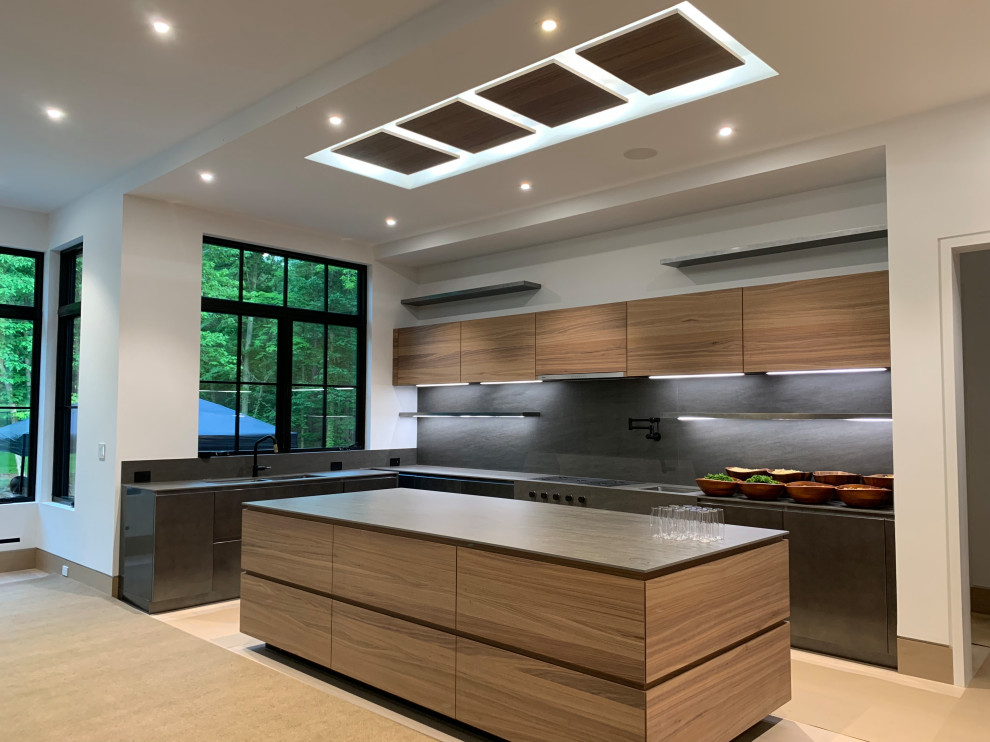 Large modern l-shaped open plan kitchen in Newark with a double-bowl sink, flat-panel cabinets, light wood cabinets, black splashback, light hardwood floors, with island and black benchtop.