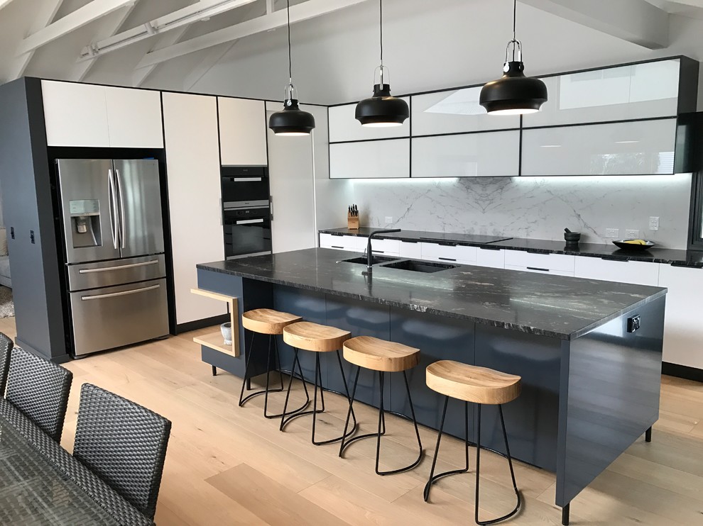 Photo of a mid-sized industrial l-shaped eat-in kitchen in Gold Coast - Tweed with a double-bowl sink, flat-panel cabinets, white cabinets, marble benchtops, white splashback, marble splashback, light hardwood floors and with island.
