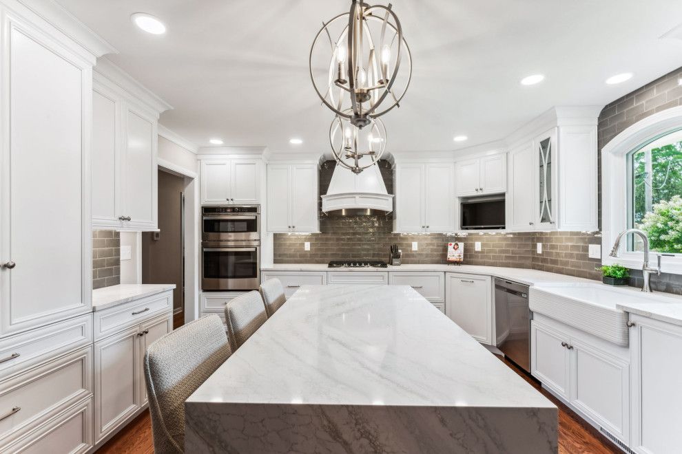 Inspiration for a mid-sized timeless l-shaped medium tone wood floor eat-in kitchen remodel in Columbus with a farmhouse sink, recessed-panel cabinets, white cabinets, quartz countertops, gray backsplash, ceramic backsplash, stainless steel appliances, an island and white countertops