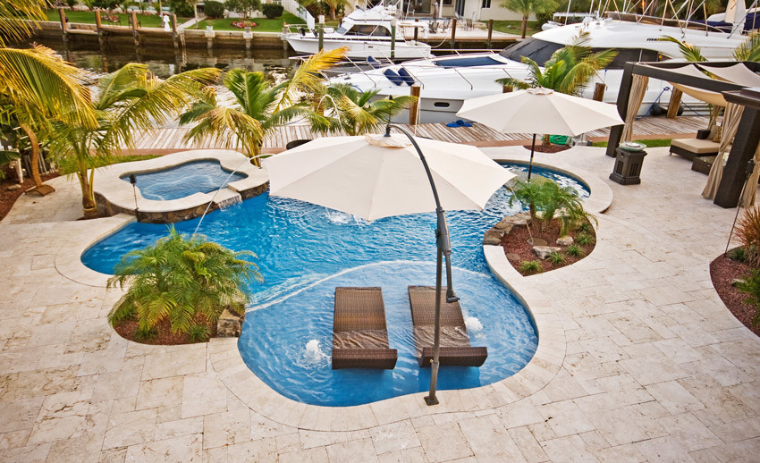 Mid-sized backyard custom-shaped pool in Miami with a hot tub and natural stone pavers.