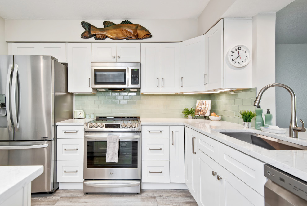 Photo of a mid-sized contemporary l-shaped separate kitchen in Tampa with a single-bowl sink, shaker cabinets, white cabinets, quartzite benchtops, green splashback, glass tile splashback, stainless steel appliances, vinyl floors, with island, grey floor and white benchtop.