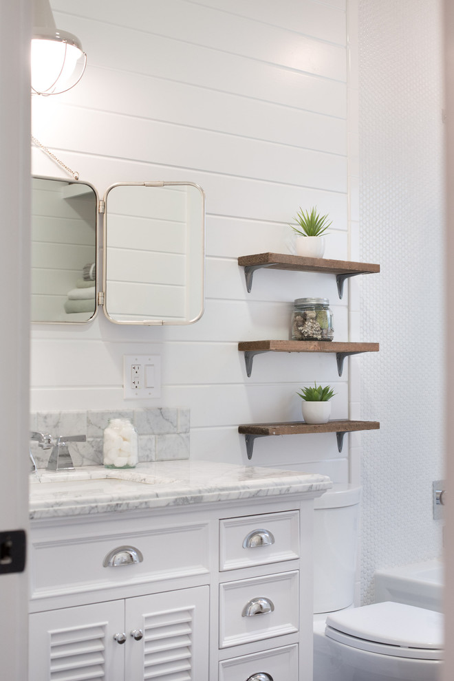 This is an example of a mid-sized scandinavian bathroom in San Francisco with an integrated sink, louvered cabinets, marble benchtops, an alcove tub, a shower/bathtub combo, a two-piece toilet, white tile, subway tile, white walls, dark hardwood floors and white cabinets.