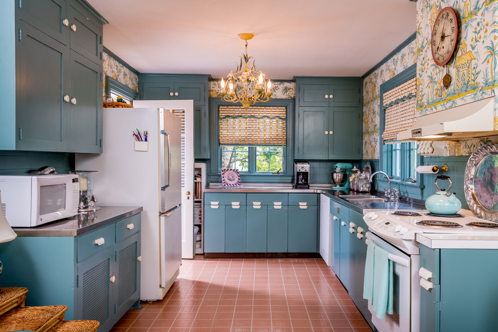This is an example of an eclectic u-shaped separate kitchen in Other with an integrated sink, shaker cabinets, blue cabinets, stainless steel benchtops, blue splashback, ceramic splashback, white appliances, terra-cotta floors and no island.