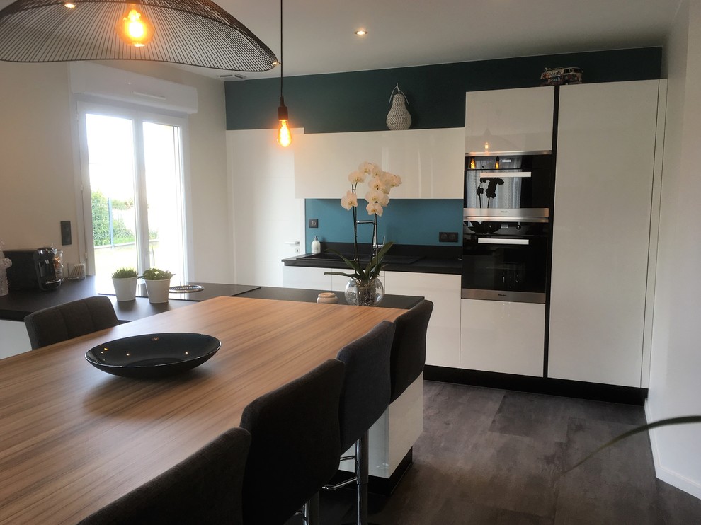Design ideas for a mid-sized modern galley open plan kitchen in Rennes with an undermount sink, flat-panel cabinets, white cabinets, granite benchtops, black splashback, black appliances, laminate floors, with island and grey floor.
