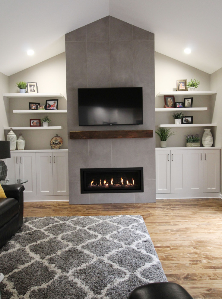 This is an example of a mid-sized transitional open concept family room in Seattle with grey walls, medium hardwood floors, a standard fireplace, a tile fireplace surround, a wall-mounted tv, brown floor and vaulted.