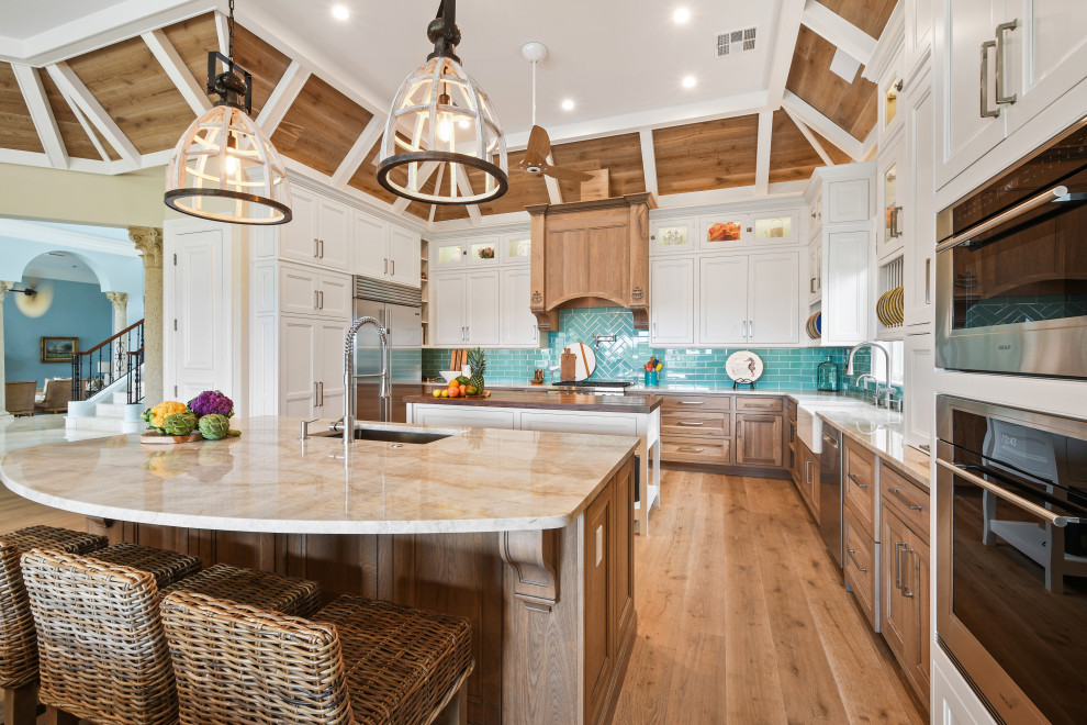 Photo of a large tropical u-shaped open plan kitchen in Other with an undermount sink, beaded inset cabinets, white cabinets, quartzite benchtops, blue splashback, glass tile splashback, stainless steel appliances, light hardwood floors, multiple islands, brown floor, beige benchtop and wood.