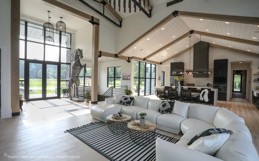 Expansive industrial open plan living room in Other with white walls, light hardwood flooring, a two-sided fireplace, a stacked stone fireplace surround, no tv and a vaulted ceiling.