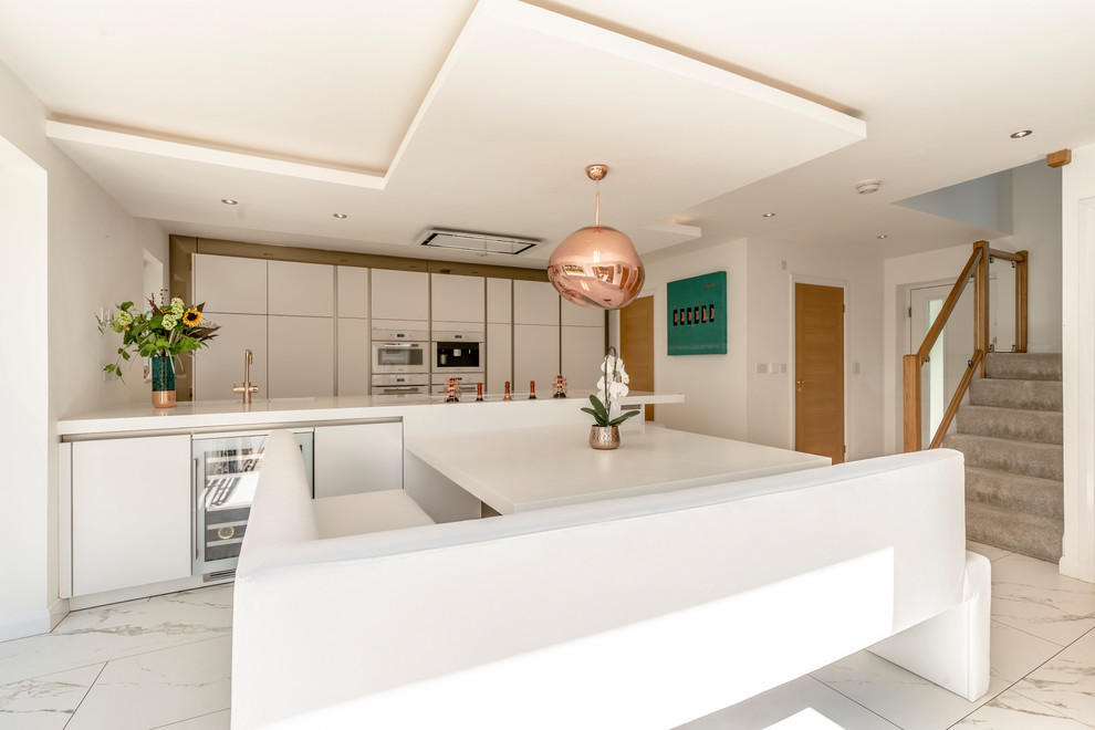 Photo of a mid-sized contemporary eat-in kitchen in Cheshire with flat-panel cabinets, white cabinets, white appliances, porcelain floors, with island, white floor and white benchtop.