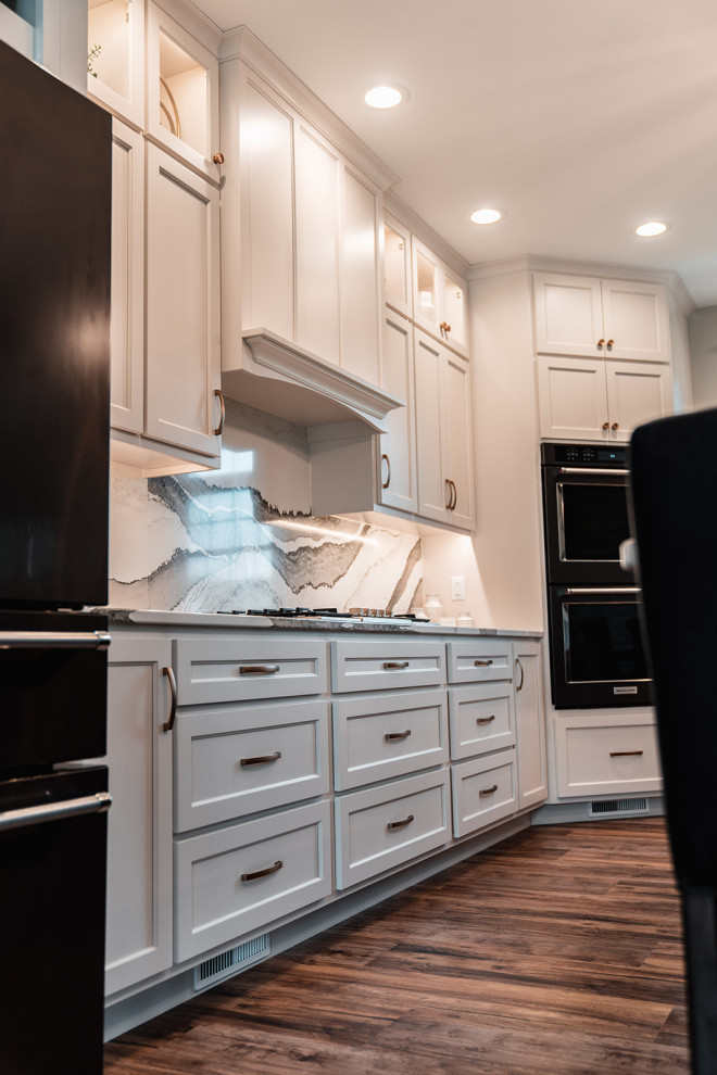 Open concept kitchen - large transitional l-shaped medium tone wood floor and brown floor open concept kitchen idea with an undermount sink, flat-panel cabinets, white cabinets, quartz countertops, multicolored backsplash, quartz backsplash, black appliances, an island and multicolored countertops