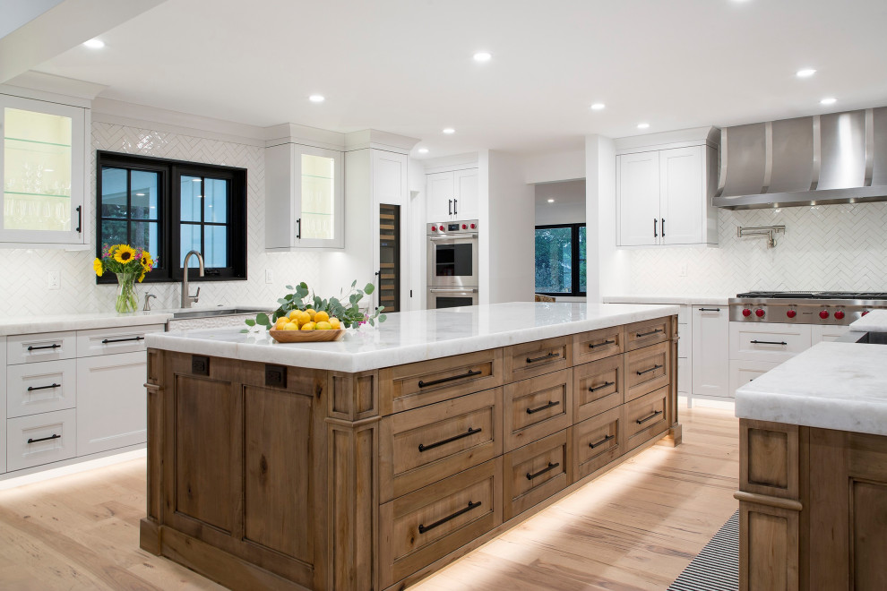 Inspiration for an expansive country galley open plan kitchen in Denver with a belfast sink, raised-panel cabinets, white cabinets, marble worktops, white splashback, ceramic splashback, stainless steel appliances, light hardwood flooring, multiple islands, beige floors and white worktops.