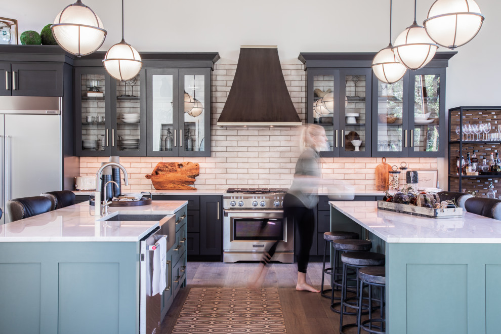 Inspiration for a large transitional u-shaped medium tone wood floor and brown floor open concept kitchen remodel with a farmhouse sink, shaker cabinets, black cabinets, quartzite countertops, white backsplash, porcelain backsplash, stainless steel appliances, two islands and white countertops