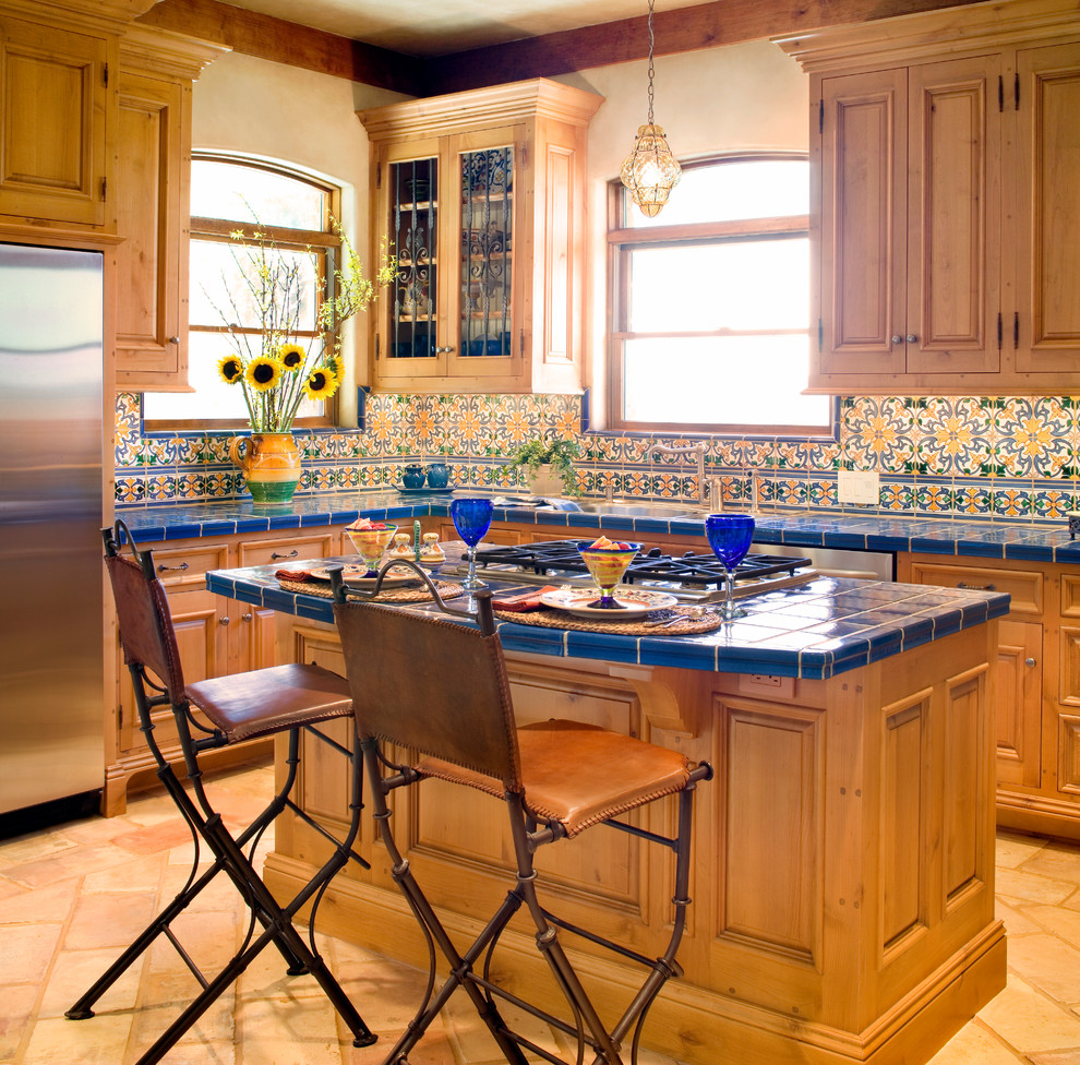 Photo of a mediterranean kitchen in Austin with raised-panel cabinets, light wood cabinets, tile benchtops, multi-coloured splashback, stainless steel appliances and blue benchtop.