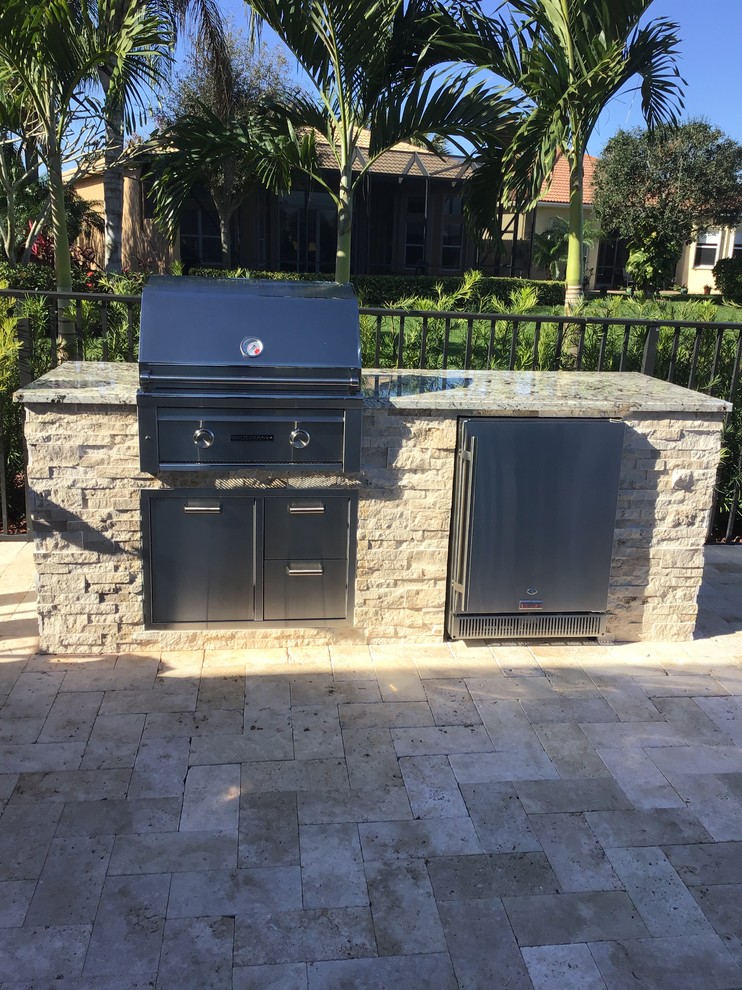 Inspiration for a transitional backyard patio in Miami with an outdoor kitchen, natural stone pavers and no cover.