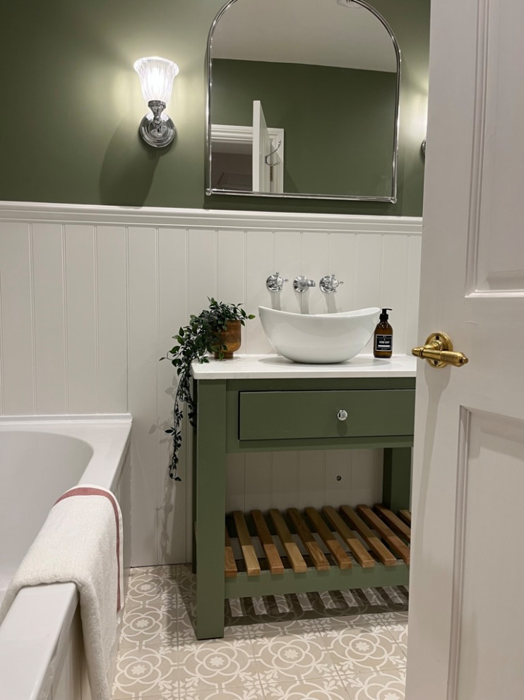 This is an example of a country master bathroom in Hertfordshire with flat-panel cabinets, green cabinets, a drop-in tub, a curbless shower, a one-piece toilet, green walls, porcelain floors, a vessel sink, solid surface benchtops, beige floor, an open shower, white benchtops, a niche, a single vanity and a freestanding vanity.