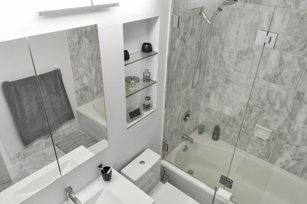 Inspiration for a mid-sized contemporary bathroom in New York with an integrated sink, white cabinets, solid surface benchtops, an alcove tub, an alcove shower, a two-piece toilet, gray tile, grey walls and marble floors.