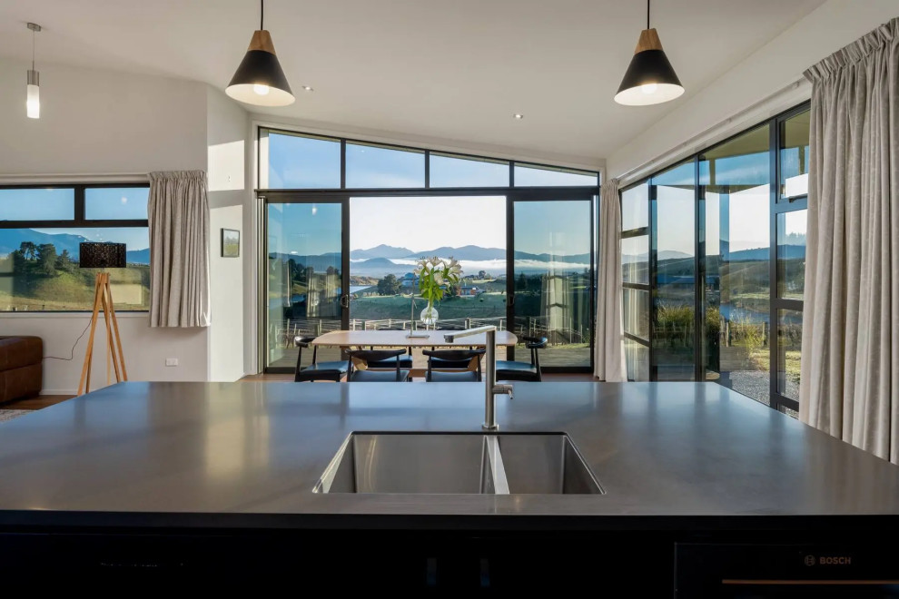 Mid-sized contemporary l-shaped eat-in kitchen in Other with an undermount sink, black cabinets, solid surface benchtops, grey splashback, mirror splashback, black appliances, medium hardwood floors, with island, brown floor, grey benchtop and vaulted.