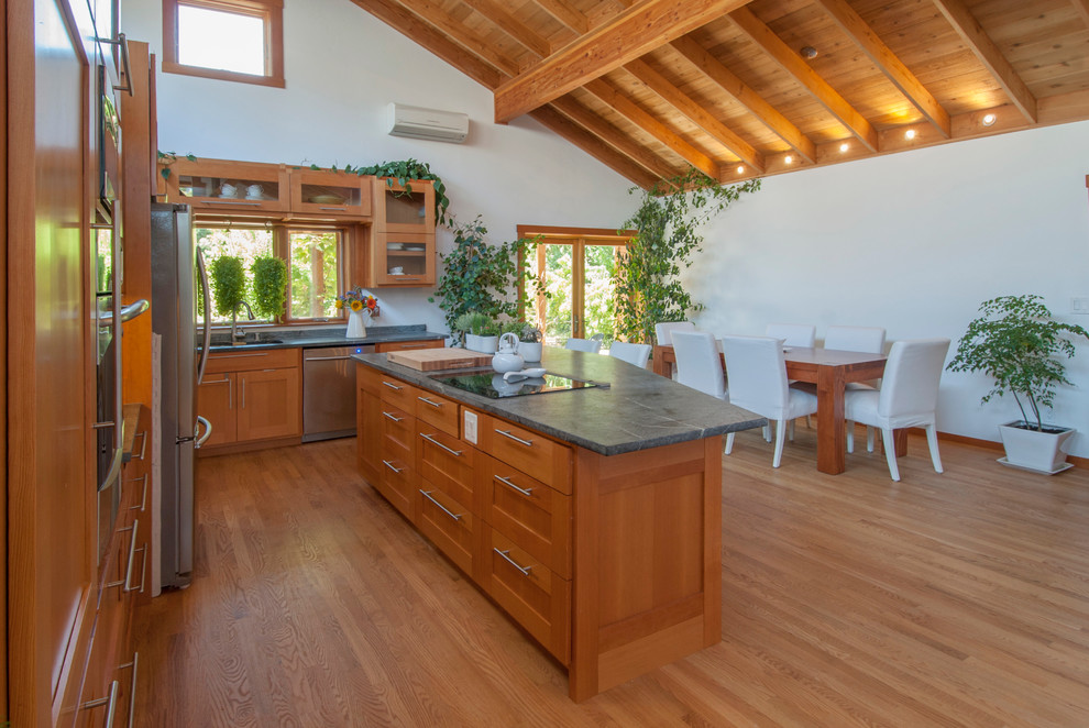 This is an example of a mid-sized country l-shaped eat-in kitchen in San Francisco with an undermount sink, shaker cabinets, medium wood cabinets, soapstone benchtops, stainless steel appliances, light hardwood floors, with island and brown floor.