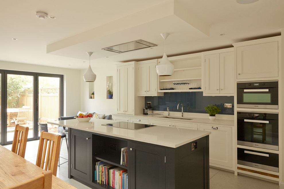 Mid-sized traditional eat-in kitchen in London with an undermount sink, shaker cabinets, white cabinets, granite benchtops, blue splashback, glass sheet splashback, stainless steel appliances, porcelain floors and with island.
