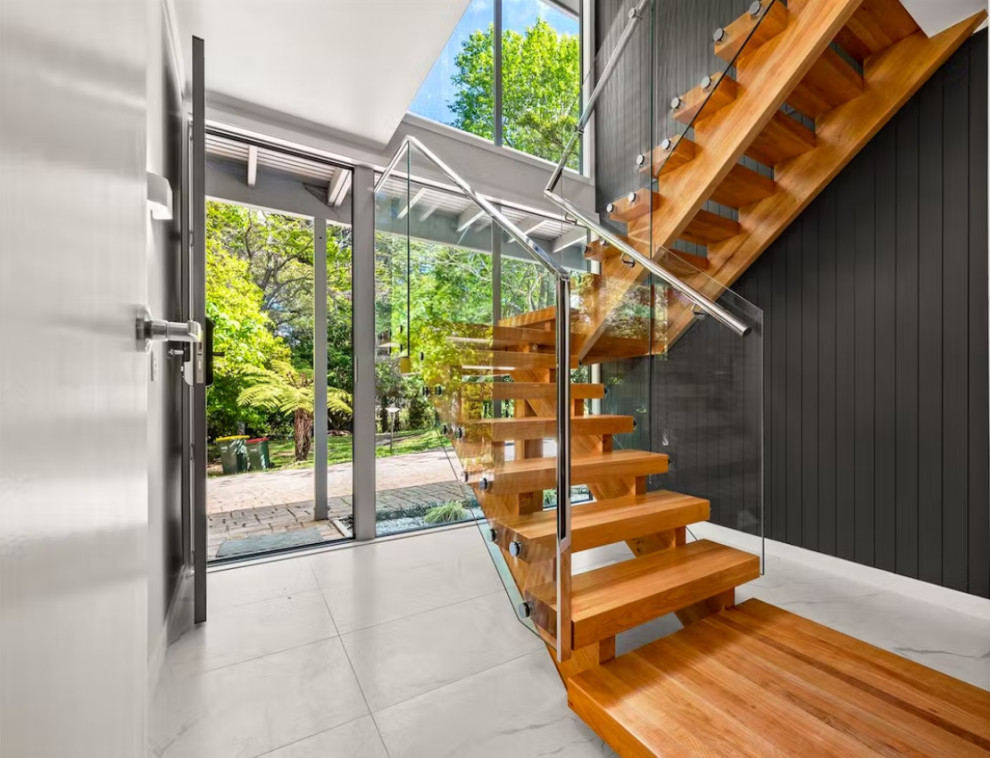 Small modern wood u-shaped glass railing staircase in Auckland with open risers and panelled walls.