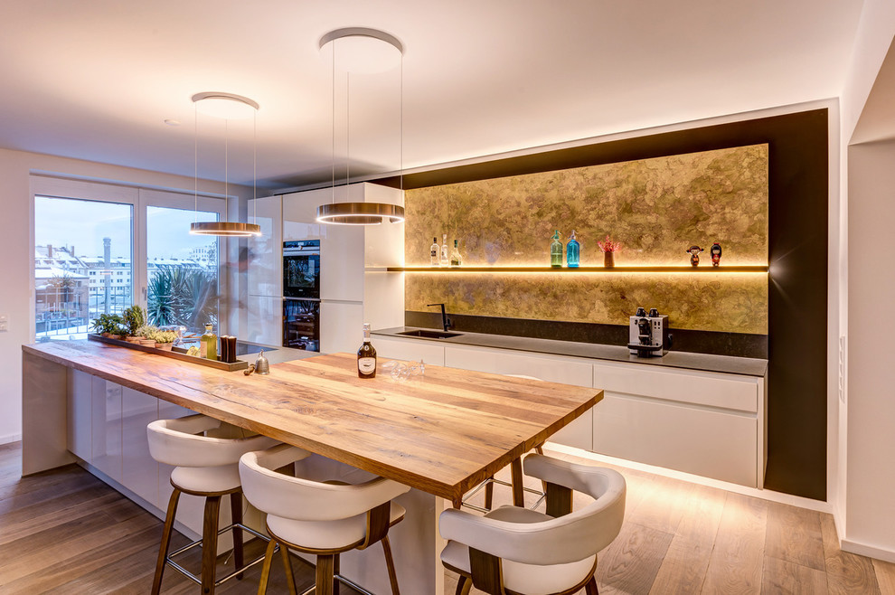 Mid-sized contemporary galley kitchen in Other with an integrated sink, flat-panel cabinets, white cabinets, yellow splashback, black appliances, medium hardwood floors, with island, brown floor and grey benchtop.