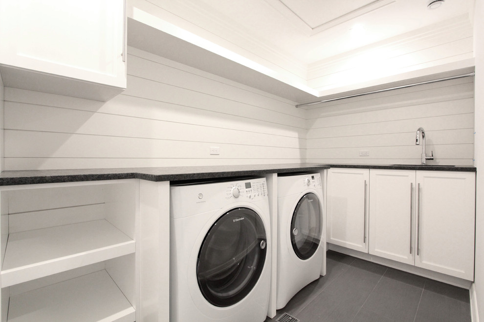 Mid-sized transitional l-shaped dedicated laundry room in New York with an undermount sink, shaker cabinets, white cabinets, white walls, slate floors, a side-by-side washer and dryer and grey floor.