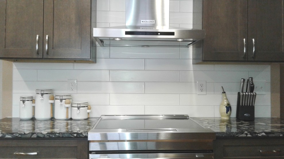 Eat-in kitchen - mid-sized transitional galley medium tone wood floor eat-in kitchen idea in Denver with an undermount sink, shaker cabinets, brown cabinets, granite countertops, white backsplash, porcelain backsplash, stainless steel appliances, a peninsula and black countertops
