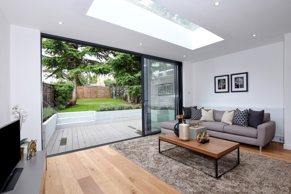 This is an example of a mid-sized modern open concept family room in London with white walls, medium hardwood floors, no fireplace and a freestanding tv.