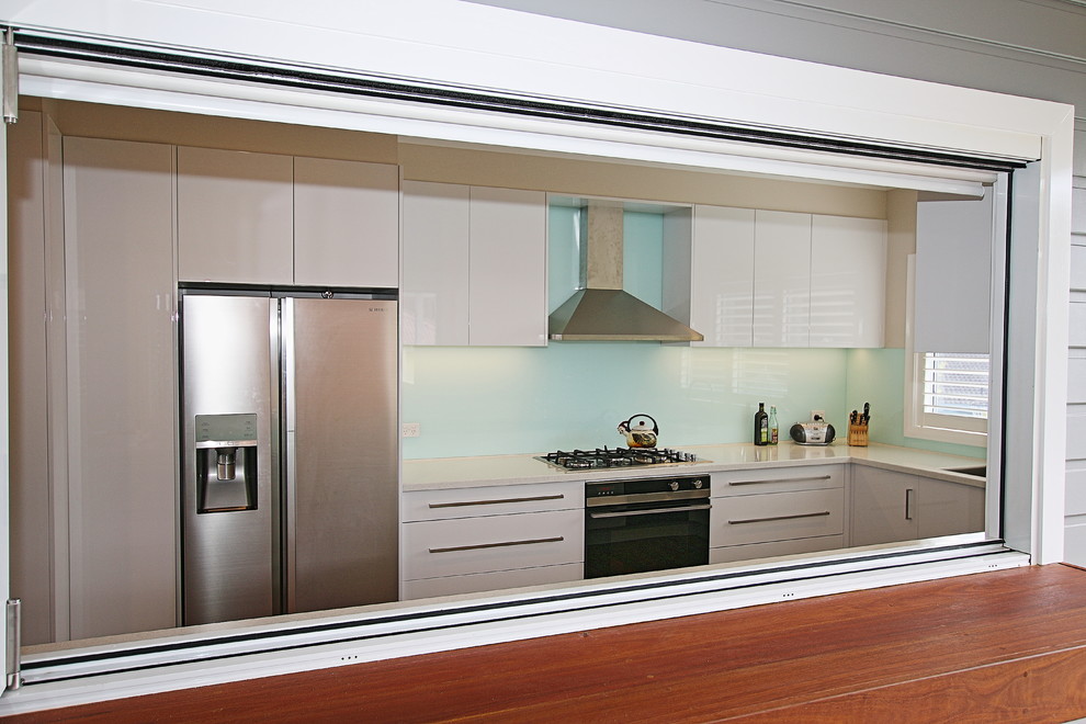 Large contemporary u-shaped kitchen pantry in Sydney with a drop-in sink, flat-panel cabinets, white cabinets, solid surface benchtops, blue splashback, glass sheet splashback, stainless steel appliances, medium hardwood floors and no island.
