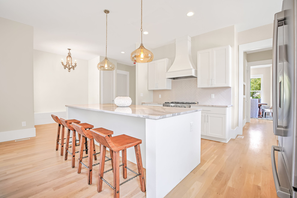 Open concept kitchen - mid-sized transitional l-shaped light wood floor open concept kitchen idea with a farmhouse sink, shaker cabinets, white cabinets, stainless steel appliances, an island, quartzite countertops, white backsplash and ceramic backsplash