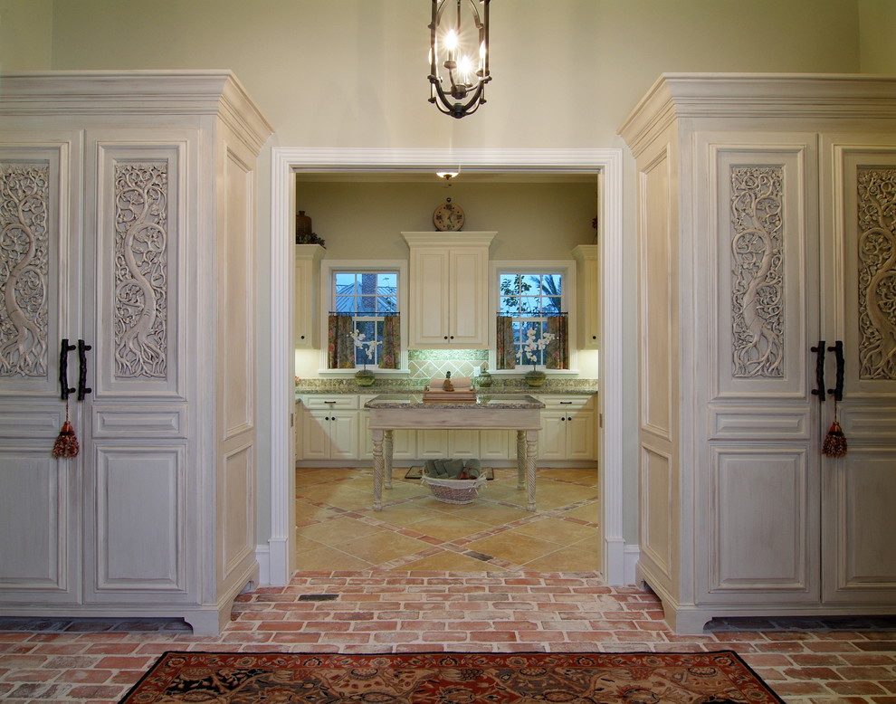 Photo of a large traditional u-shaped utility room in Houston with a farmhouse sink, raised-panel cabinets, granite benchtops, beige walls, travertine floors and beige cabinets.