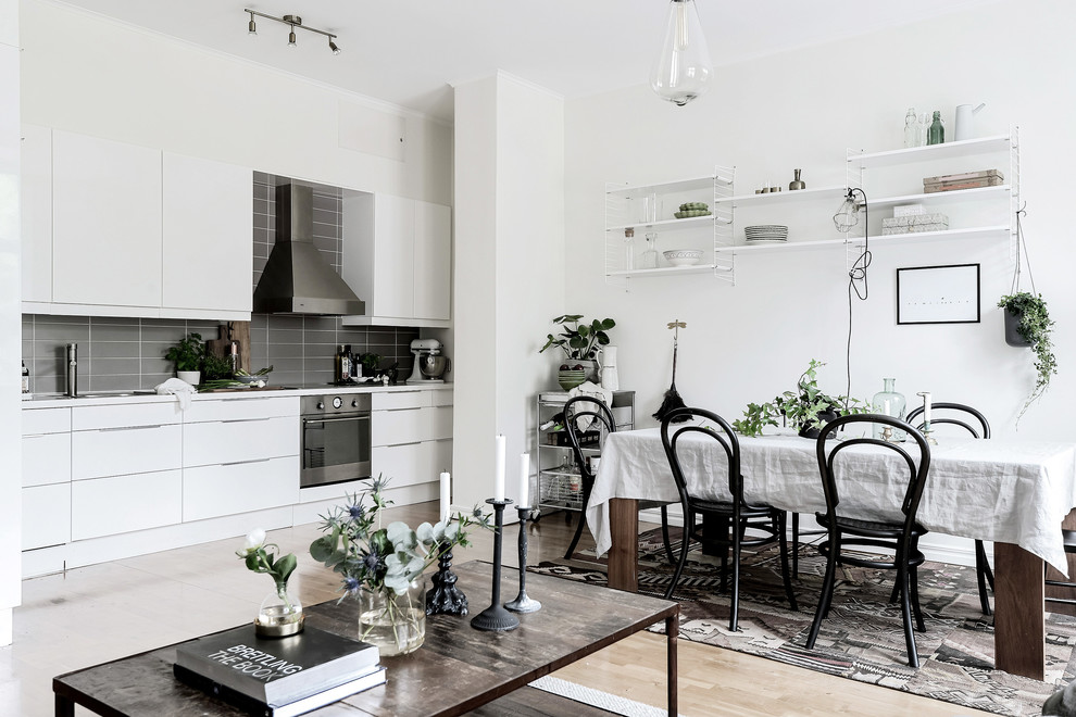 This is an example of a scandinavian single-wall eat-in kitchen in Gothenburg with flat-panel cabinets, light hardwood floors, no island, beige floor, grey splashback, stainless steel appliances and slate splashback.
